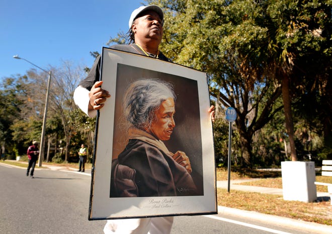 An unidentified woman marches holding a portrait of Rosa Parks along E. University Avenue in honor of Dr. Martin Luther King, Jr., during the King Celebration 2015 National Holiday Kick-Off event Monday, January 19, 2015. (Doug Finger/The Gainesville Sun)