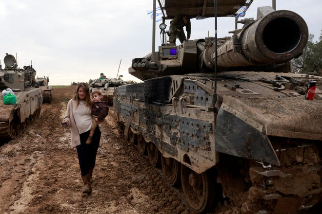 The wife of an Israeli soldier carries her child past a tank, as she visits her husband upon his return from a mission in the Palestinian territory on January 28, 2024, amid ongoing battles between Israel and the Palestinian Hamas militant group.