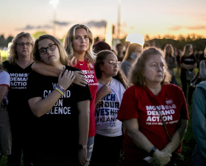 Members of the Northern Palm Beach County chapter of Moms Demand Action, Kristen Azari, with her daughters Emma, 12, and Maya, 10, and Michele Erbrick, right, attend an interfaith ceremony honoring the memory of those who lost their lives at MSD High School last year, Thursday evening inside Pine Trails Park, in Parkland, Florida. [RICHARD GRAULICH/palmbeachpost.com]